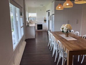 Une cuisine moderne avec des meubles blancs, une table à manger en bois et des luminaires suspendus.