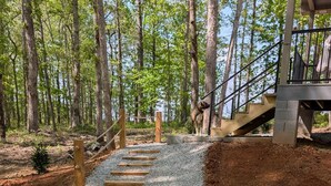 Un chemin de gravier mène à un escalier en bois situé dans une zone boisée.