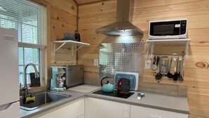 Une cuisine compacte équipée d’un évier, d’une machine à café, d’une bouilloire, d’un four à micro-ondes et d’un pare-éclaboussures en métal.