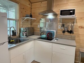 Een praktische keuken met een spoelbak, een koffieapparaat, een waterkoker, een magnetron en een metalen spatwand.