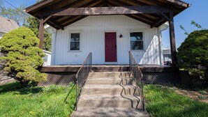 A white building with a red door, a porch, and a staircase leading to the entrance. - The Bungalow On Fife only 11 minutes from WEC (Wilmington)