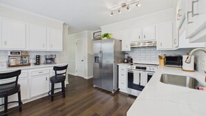 Una cocina moderna con armarios blancos, un refrigerador de acero inoxidable, horno empotrado y una isla grande con pileta.