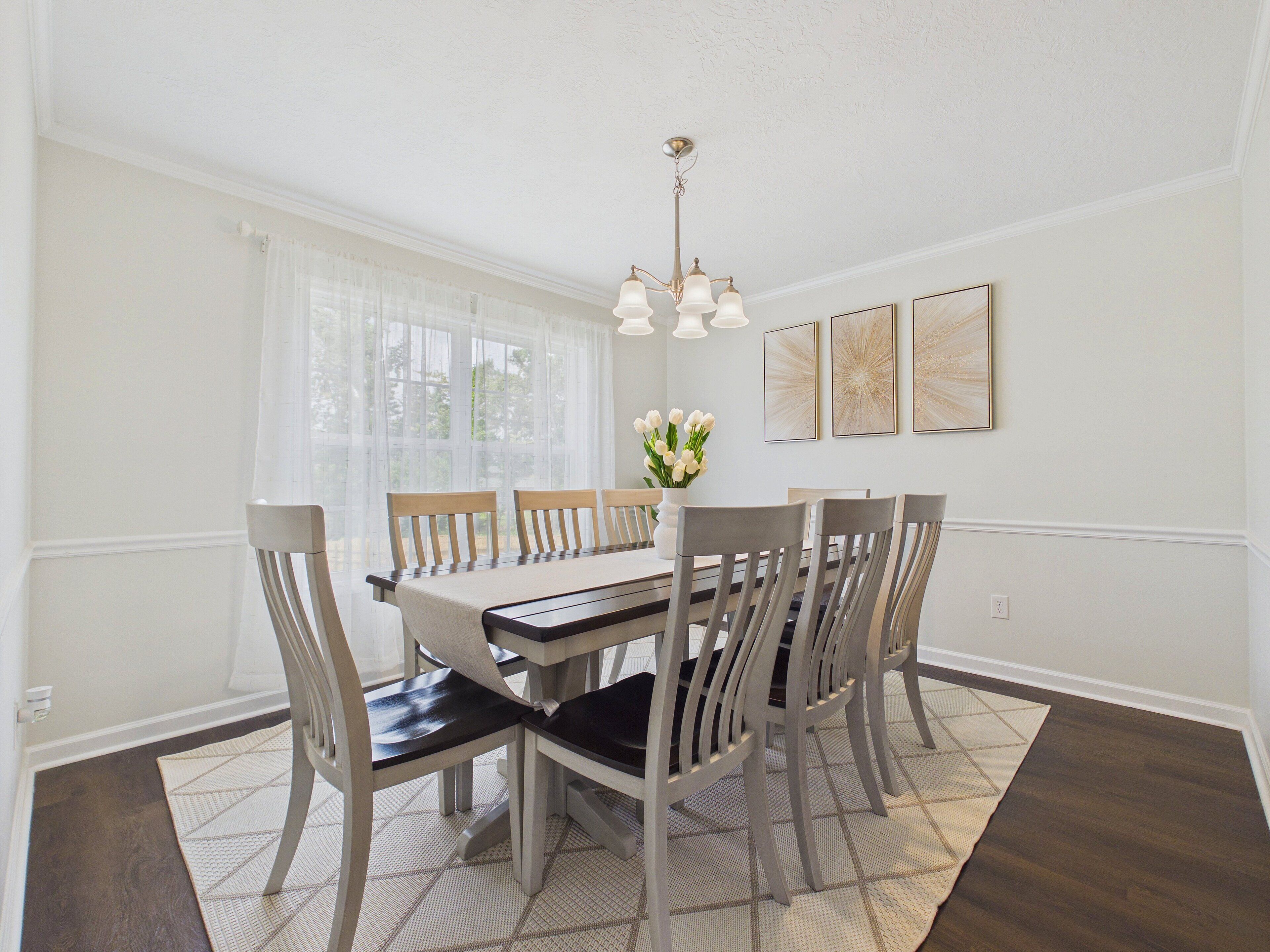 Une salle à manger avec une grande table, six chaises, un lustre et trois tableaux accrochés au mur.