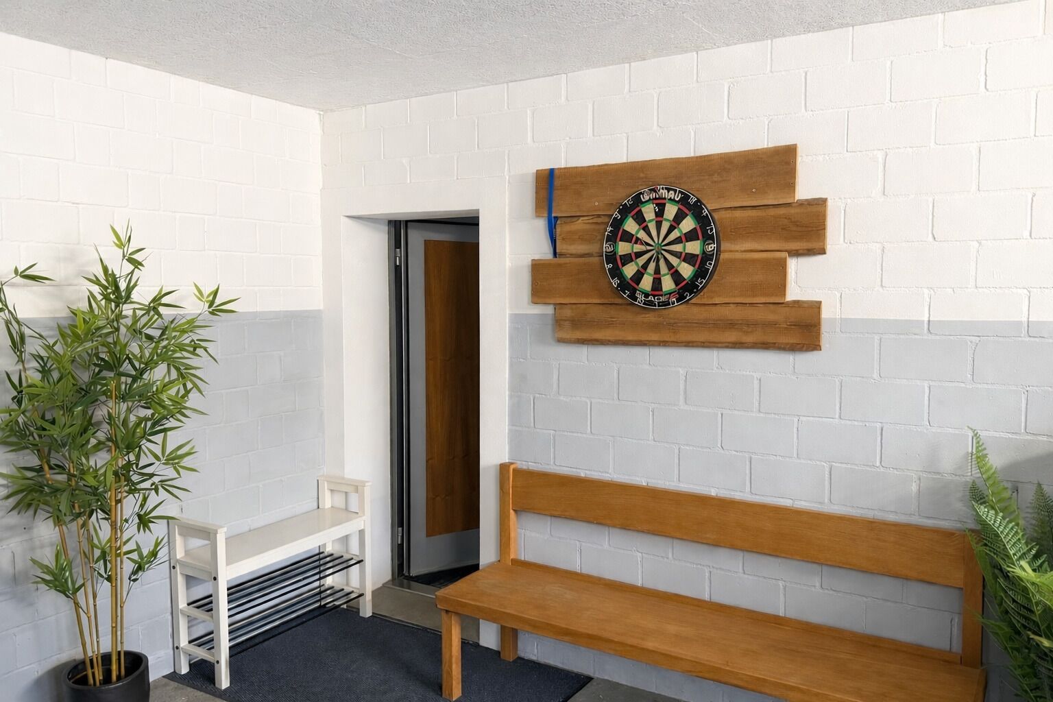 Ein Raum mit Dartscheibe, einer Holzbank, einem kleinen Tisch und einem Blumentopf.