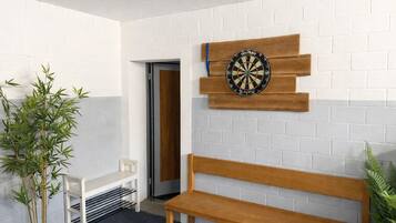 Ein Raum mit Dartscheibe, einer Holzbank, einem kleinen Tisch und einem Blumentopf.