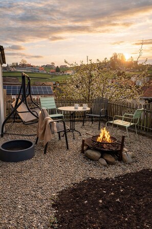 An outdoor patio with a fire pit, seating area, and solar panels in the background.