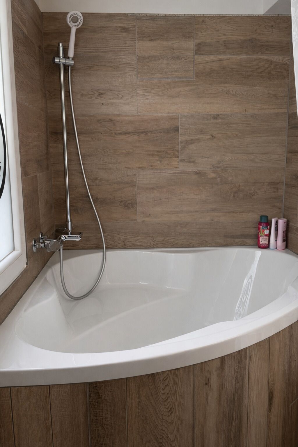 Une salle de bain moderne avec une baignoire sur pieds, une douchette et des panneaux muraux en bois.