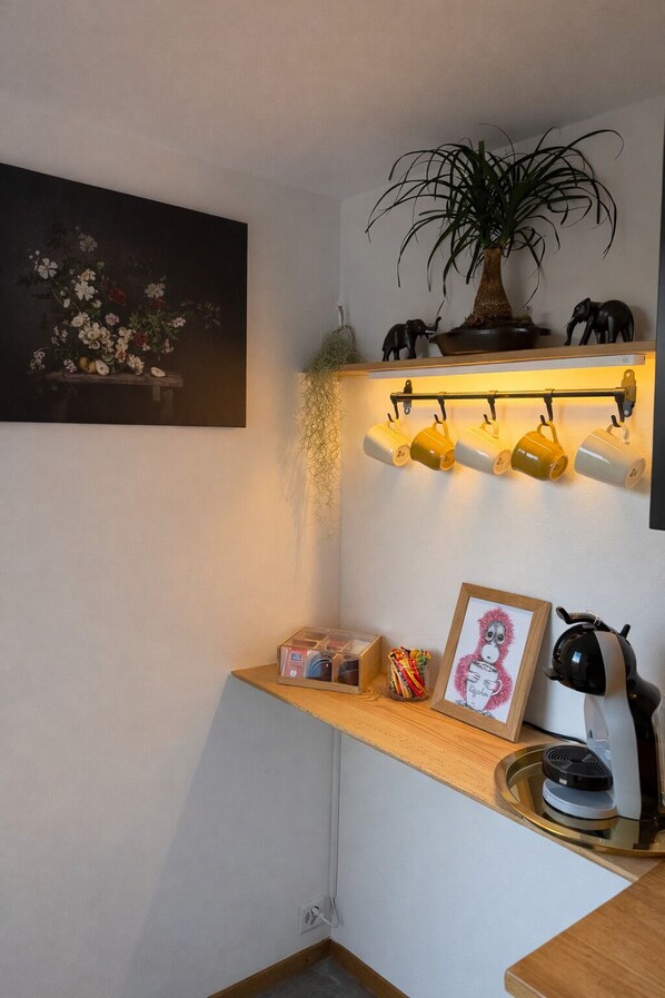 A corner of a room with a shelf holding mugs, a framed picture, a potted plant, and a small statue.