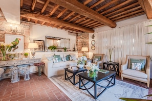 A rustic living room with exposed wooden beams, a white sofa, a coffee table, and decorative items. - Villa in Lucca With Winery and Vineyard Views (Lucca)
