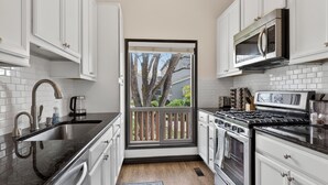A modern kitchen with white cabinetry, a stainless steel range, a microwave, and a large window with a view of trees. - Golf villa located in Continental Country Club (Flagstaff)