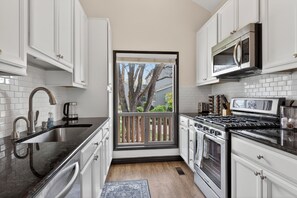 A modern kitchen with white cabinetry, a stainless steel range, a microwave, and a large window with a view of trees. - Golf villa located in Continental Country Club (Flagstaff)