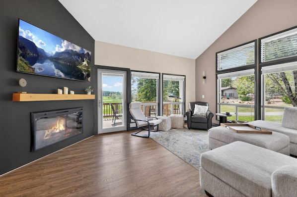 A modern living room with a fireplace, a large TV, and a view of a deck and greenery. - Golf villa located in Continental Country Club (Flagstaff)