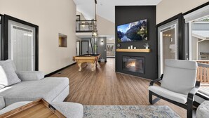 A modern living room with a pool table, a fireplace, a mounted TV, and a balcony with a railing. - Golf villa located in Continental Country Club (Flagstaff)