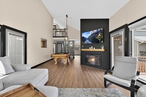 A modern living room with a pool table, a fireplace, a mounted TV, and a balcony with a railing. - Golf villa located in Continental Country Club (Flagstaff)