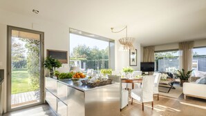 Eine moderne Küche mit einer großen Kochinsel, ein Essbereich mit Tisch und Stühlen sowie ein Wohnbereich mit Sofa und Fernseher.