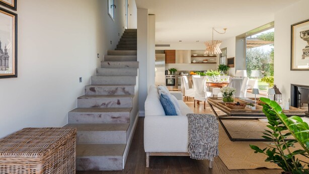 Ein modernes Interieur mit Treppe, einer Sitzecke, einem Esstisch und einer Küche im Hintergrund.