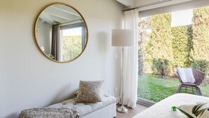 Ein Schlafzimmer mit großem Fenster, einem runden Spiegel, einer Stehlampe, einer Couch und einem Sessel.