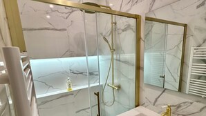 A modern bathroom with a glass-enclosed shower, a white sink with gold fixtures, and marble-patterned walls. - Luxury Apartment Paris Trocadero- 2 bedrooms 80m2 (Paris)