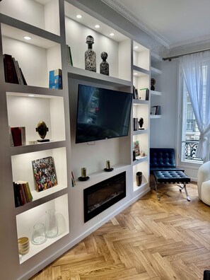 Una sala de estar moderna con una televisión de pantalla plana, estanterías empotradas, chimenea y un sofá azul.