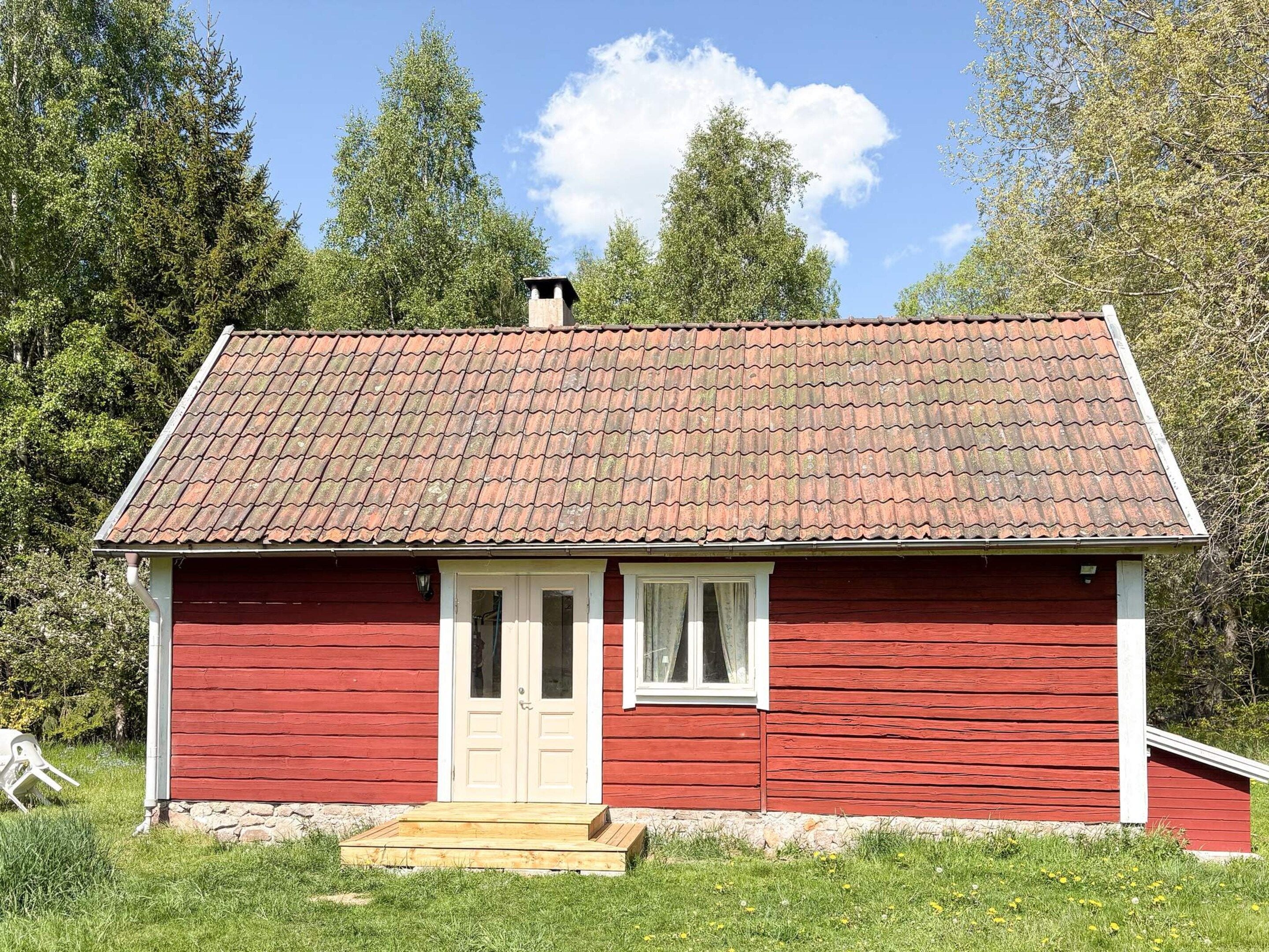 Ett rött trähus med ett tak täckt av tegelpannor, en ytterdörr och ett litet fönster.