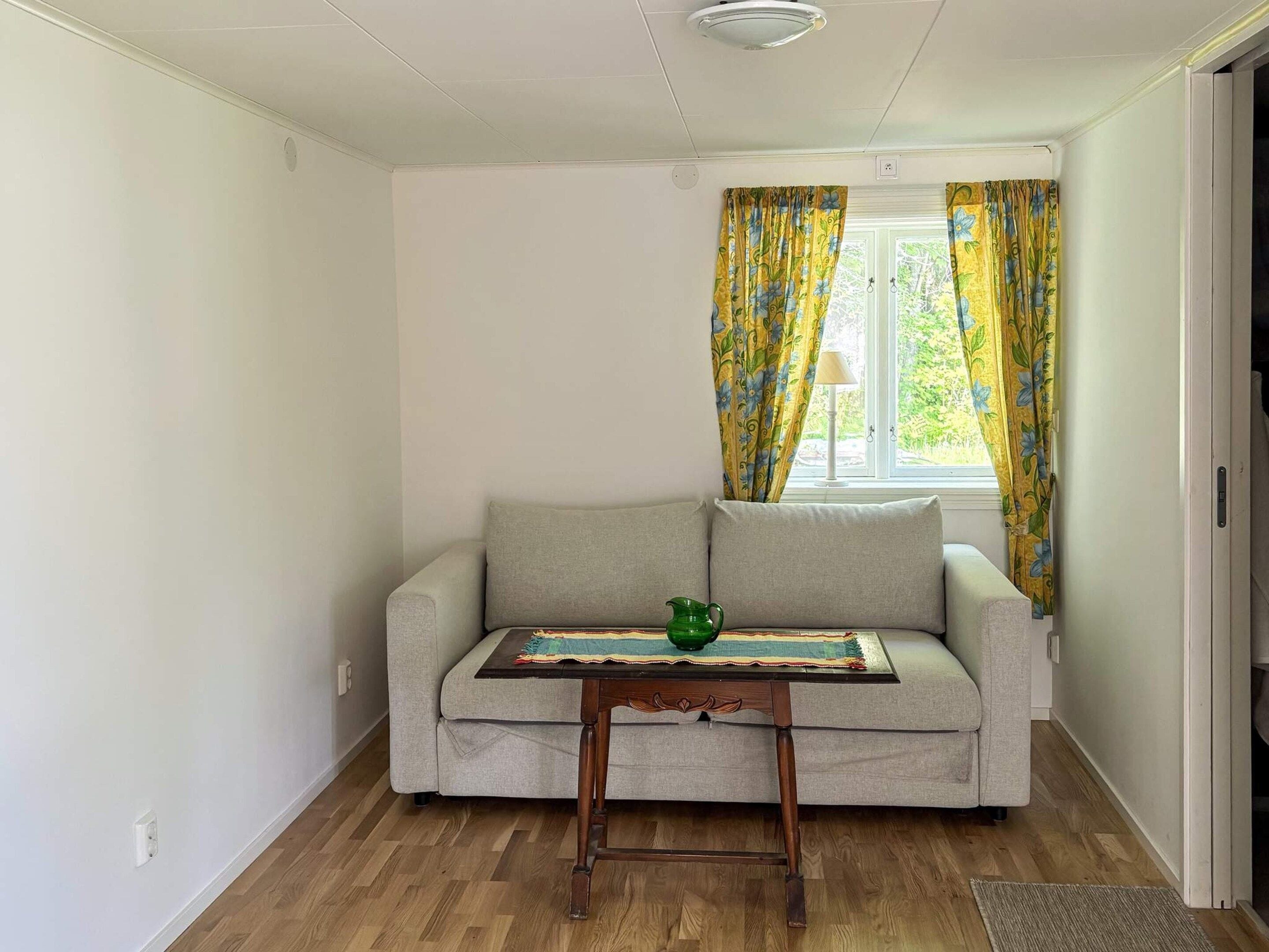 Una habitación con un sofá, una mesita de madera y un ventanal con cortinas.