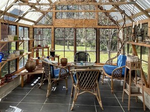 Ein Wintergarten mit Glasdach, Korbmöbeln und Regalen mit verschiedenen Gegenständen.