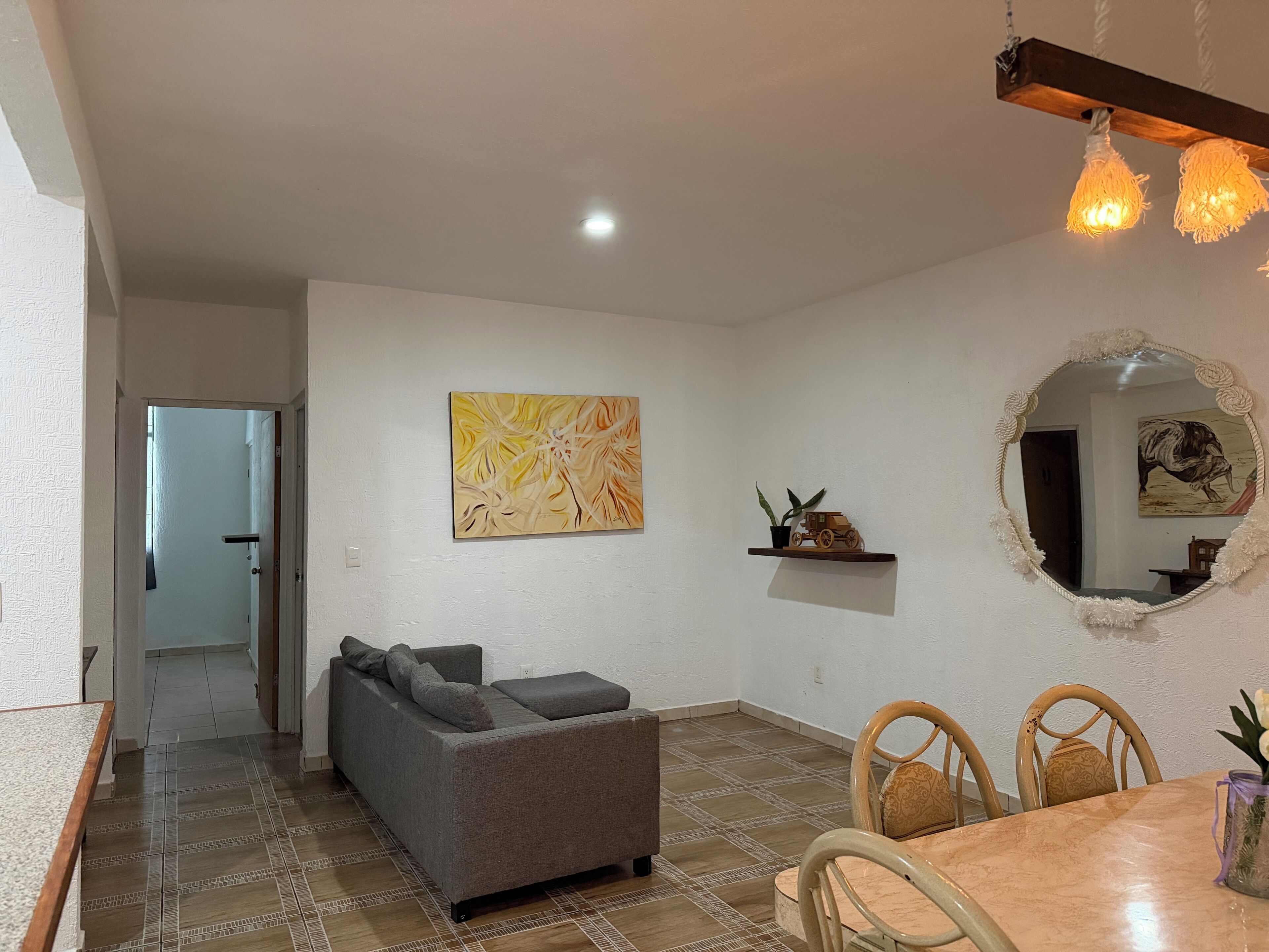 A living room with a sofa, a dining table with chairs, a mirror, and a painting on the wall.