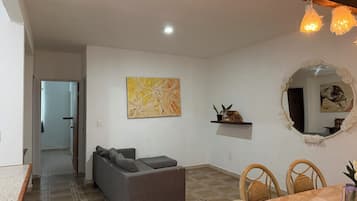 A living room with a sofa, a dining table with chairs, a mirror, and a painting on the wall.