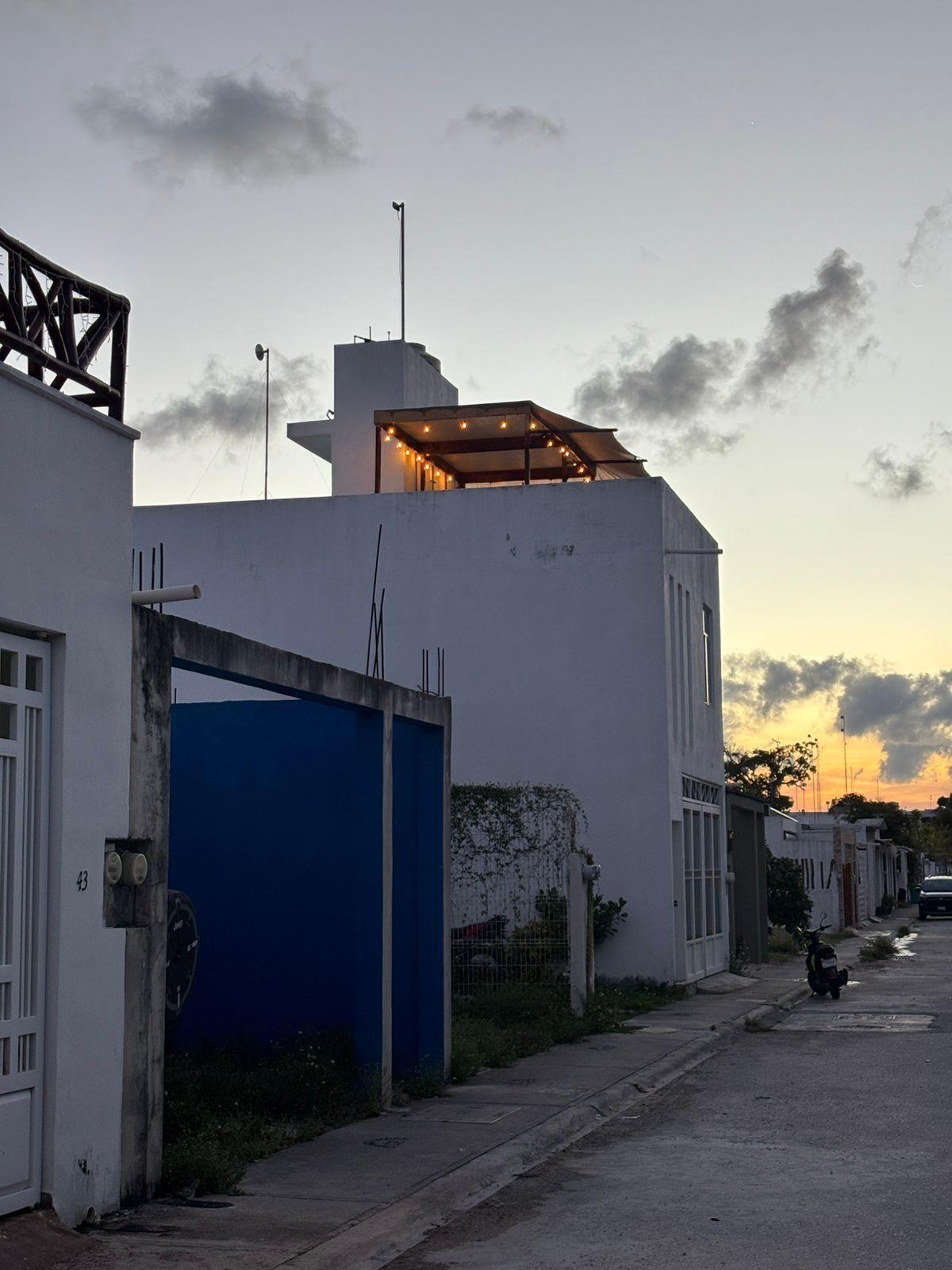 Une rue résidentielle avec un portail bleu, des bâtiments blancs et un ciel dégagé.