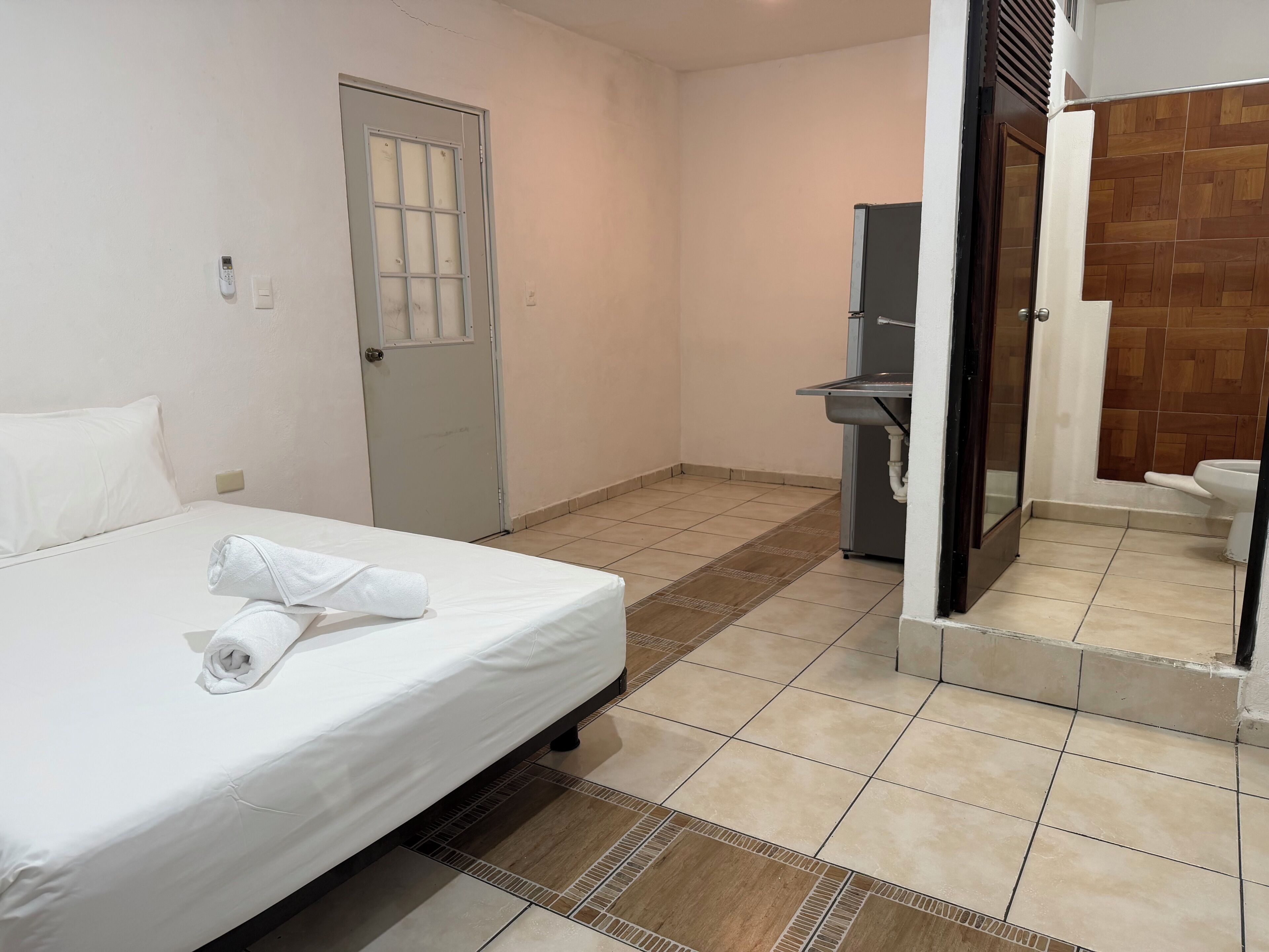 A hotel room with a bed, a door, a sink, and a shower area.