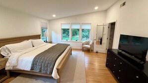 Een slaapkamer met een bed, een stoel, een kast, een televisie en ramen met uitzicht op groen.