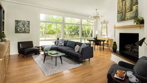 Een woonkamer met een hoekbank, een salontafel, een open haard en een eethoek met een tafel en stoelen.