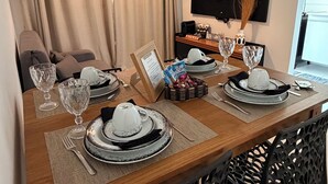 A dining area with a wooden table set for four, a television mounted on the wall, and a sofa in the background. - Apartment Prox.As Aruna and Atalaia beaches and airport 5 minutes from the apartment. (Aracaju)
