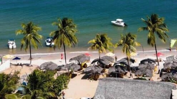 A beach with palm trees, umbrellas, and a boat on the water. - Apartment Prox.As Aruna and Atalaia beaches and airport 5 minutes from the apartment. (Aracaju)