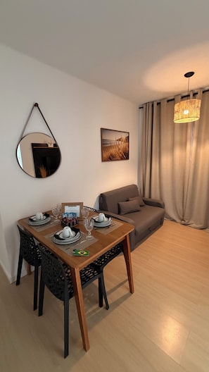 A dining area with a table set for two, a sofa, a mirror, a painting, and a chandelier.