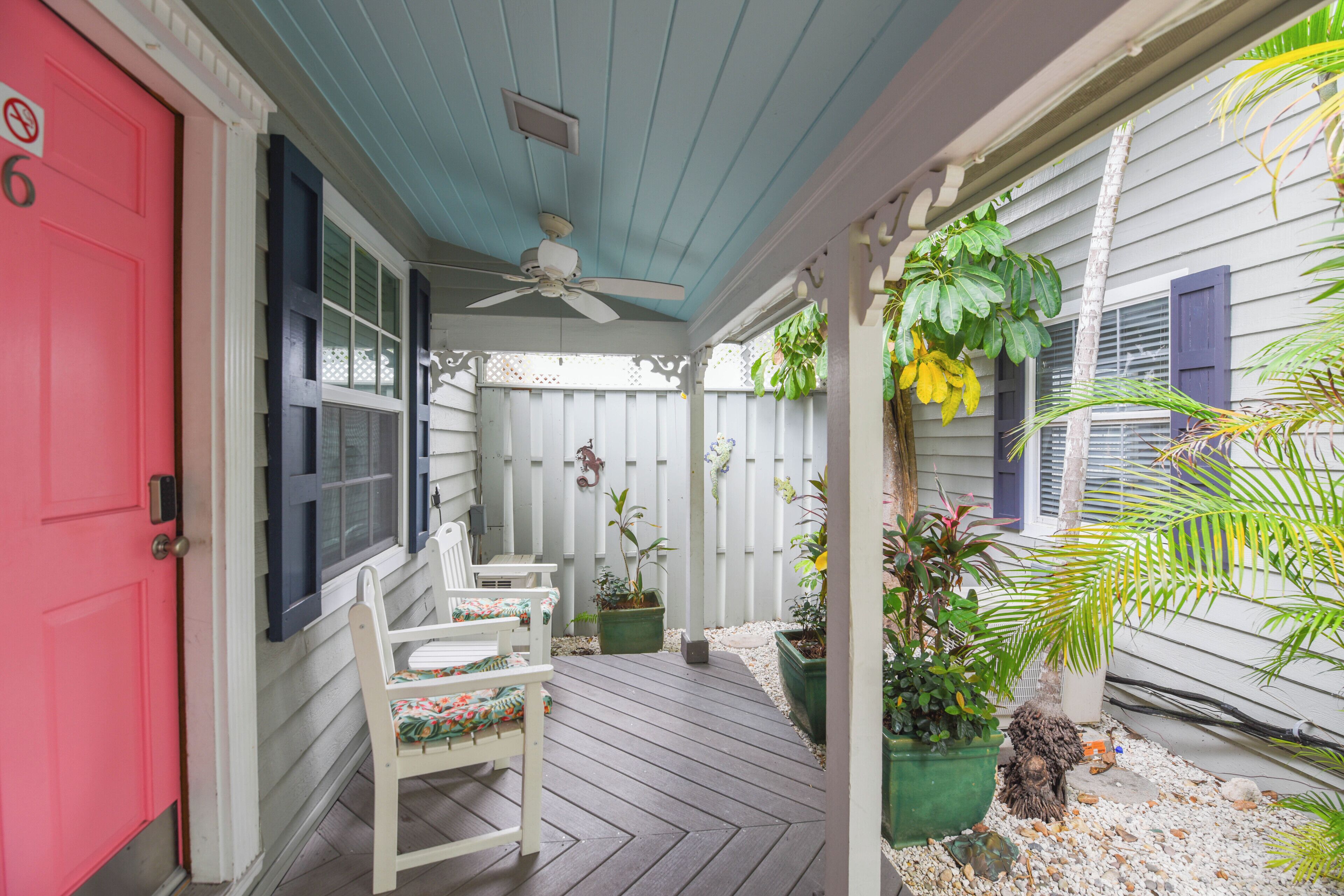 A porch with a ceiling fan, a red door, and a seating area with chairs.