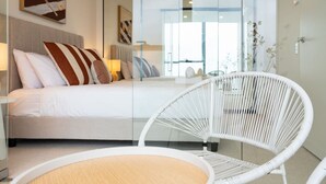 Een moderne hotelkamer met een bed, een witte rieten stoel en kunstwerken aan de muren.