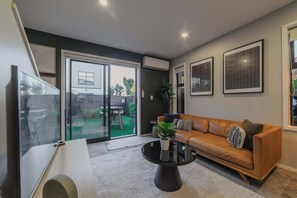 A modern living room with a sofa, a coffee table, and a sliding glass door leading to a patio. - Cozy & Stylish Central City Retreat (Christchurch)