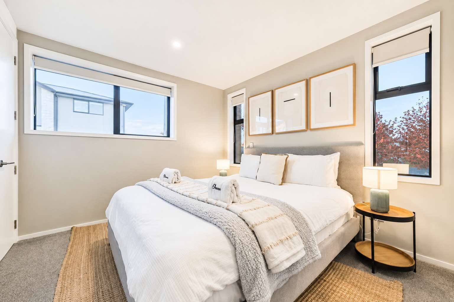 A hotel room with a large bed, a bedside table with a lamp, and a window with a view of trees.