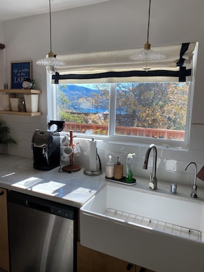 Eine Küche mit einem Edelstahl-Geschirrspüler, einer Kaffeemaschine, einem Papiertuchspender und einem Fenster mit Blick auf einen See und Berge.