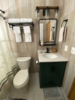 Ein Badezimmer mit Toilette, Waschbecken, Spiegel, Handtuchhalter und einer Duschkabine.