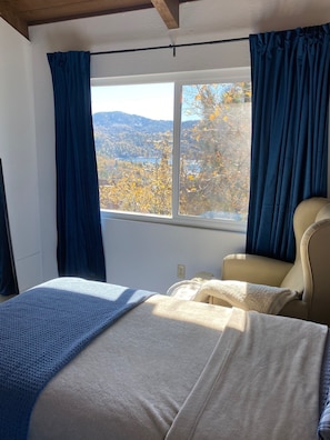 Ein Schlafzimmer mit Bett, Stuhl, Fenster mit Vorhängen und Blick auf Herbstlaub.