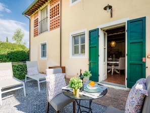 Eine Terrasse mit Sitzgelegenheiten im Freien, ein Tisch mit einer Flasche und eine grüne Tür, die zu einem Zimmer führt.