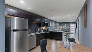 A modern kitchen with stainless steel appliances, dark cabinetry, and a dining area with a wooden table and chairs. - Luxury 2 BD Apartment (Festus)