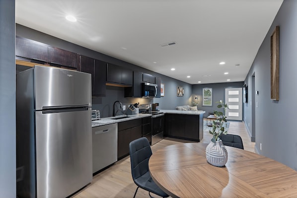 A modern kitchen with stainless steel appliances, dark cabinetry, and a dining area with a wooden table and chairs.