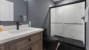 A modern bathroom with a large mirror, two sinks, a shower enclosure, and a toilet. - Luxury 2 BD Apartment (Festus)