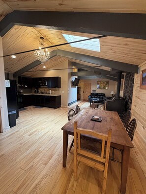 Ein geräumiger Loftsraum mit Holzboden, einem Esstisch mit Stühlen, einer Chandelier, einem Kamin und einem Oberlicht.