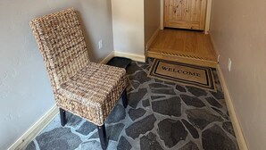 A room with a stone-patterned floor, a wicker chair, a wooden door labeled 'Box Canyon Retreat,' and a welcome mat. - Box Canyon / Downtown Ouray / 2BR / Hot Springs / AC (Ouray)