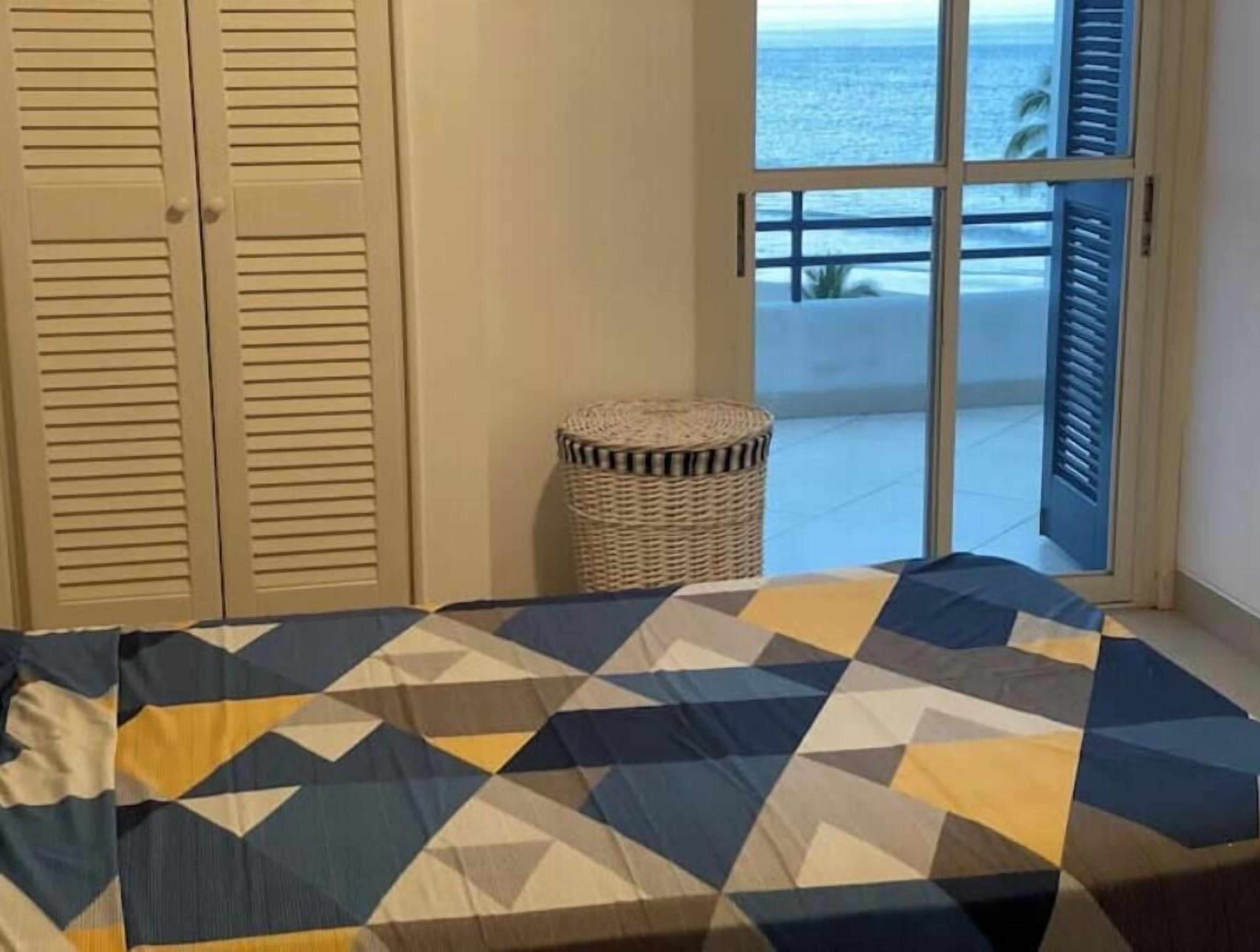A bedroom with a bed, a window with a view of the sea, a wicker basket, and a set of sliding doors.