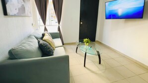 En stue med en sofa, et sofabord i glas, et fjernsyn og en dør.